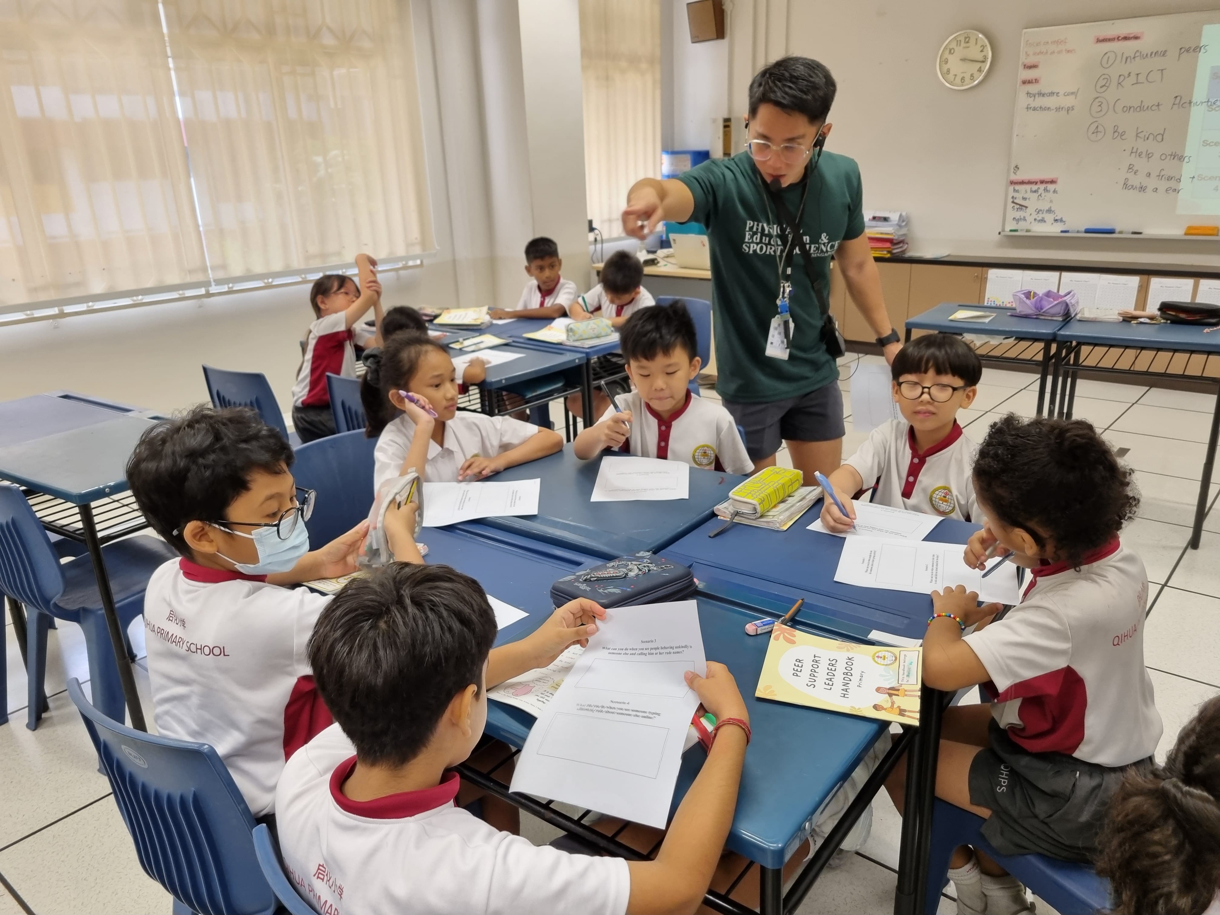 Teacher giving instructions to a group of students seated at the students' tables and chairs